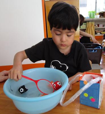 子どもが椅子に座って、洗面器の中に泳いでいる金魚をすくっている。。